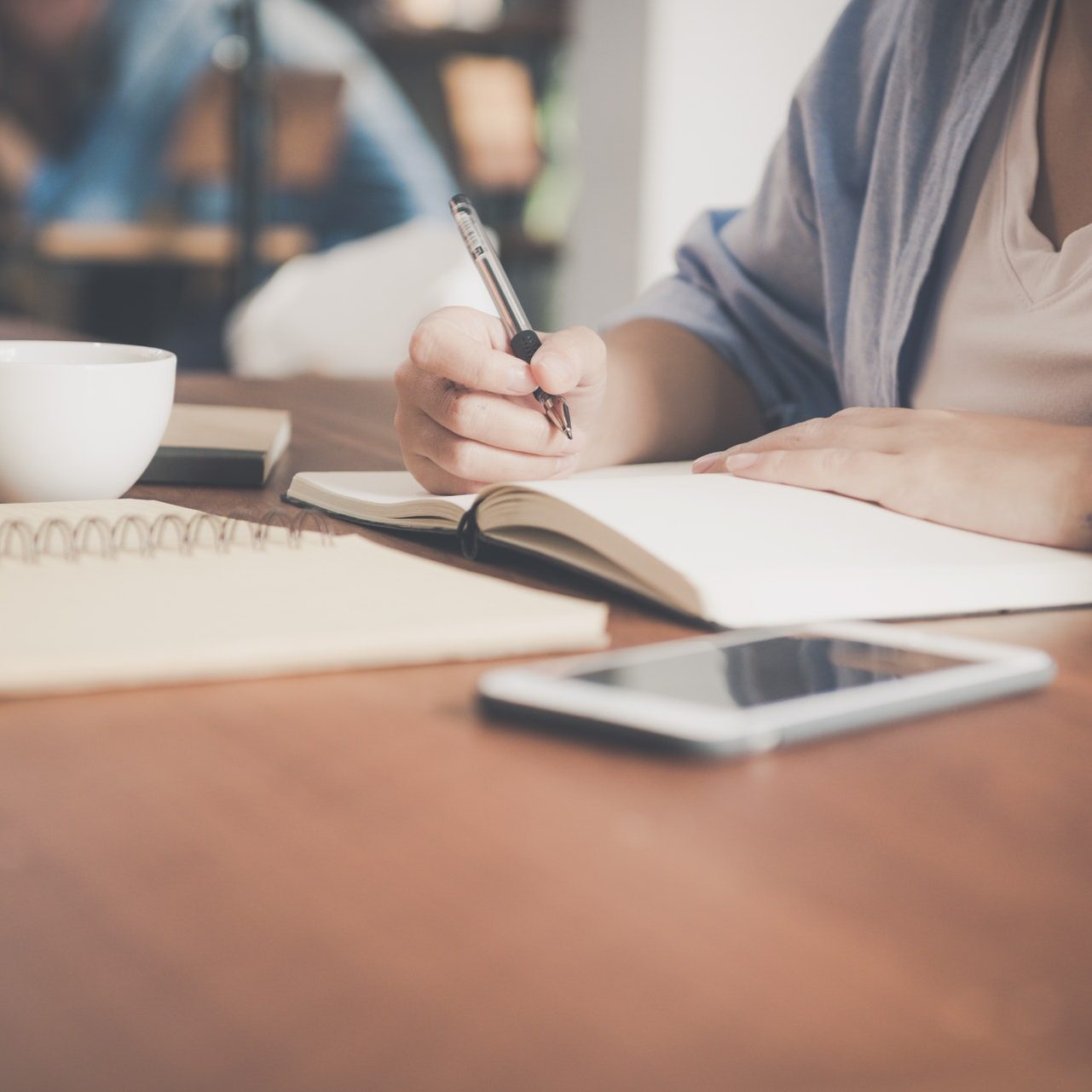 woman-writing-on-a-notebook-beside-teacup-and-tablet-733856